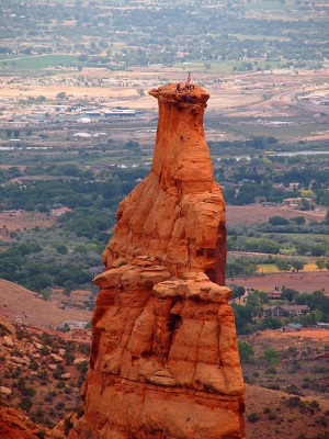 [This view shows the skinny side of the rock (rather than the flat face) and an American flag with little specks of people around it are visible. In the background are the trees and buildings of Fruita, Colorado.]