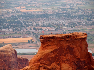 [The long flat face of the rock with the blue square and red and white stripes clearly visible as the wind unfurled the flag. People are also clearly visible atop the rock.]