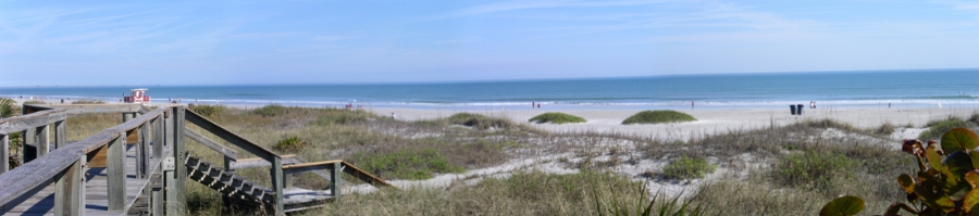 [Boardwalk on the left with steps leading to the sand in middle left. Rest of image is the grassy dunes, the beach and the ocean.]