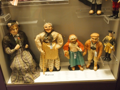 [Soft-sculpture male and female peasant dolls in the middle with one military dressed doll on the right and one well-dressed woman doll on the left.]