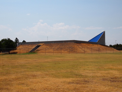 [Earth is built up on the sides so no walls are seen. An opening (the door) is visible in the grass as is a small section of triangular roof.]