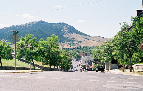 [Looking down Lawrence Street which is lined with trees on either side. It goes down a slight hill then upward. In the distance not far from the city is a tall mostly evergreen covered mountain.]