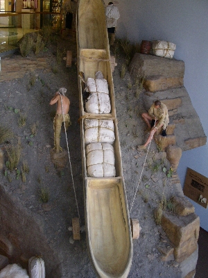 [A diorama showing a long canoe-like boat with wheels in front and back and two men, one on each side, pulling a rope to roll the canoe up the hill.]