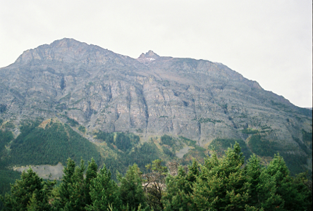 [A huge hunk of rocky mountain with a number of vertical crevices along its face. There is one section of the mountain which is like a little crown on the top.]