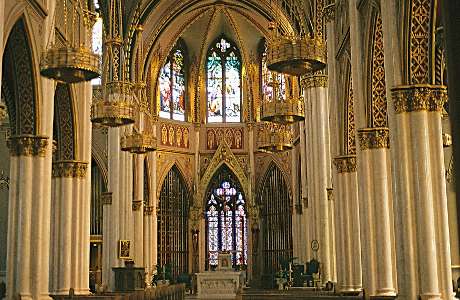 [A very ornate interior with marble columns and gold in the many arches. There are stained glass windows both behind the altar and on the second level above it. Gold chandeliers hang from the ceiling.]