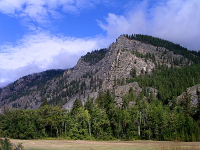 [A relatively short mountains which has many many rock crevices leading to its tree-topped summit. Also plenty of evergreens at the ground level near the brown river.]