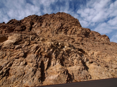 [Looking up at craggy, vegetationless rock framed by white and blue skies.]