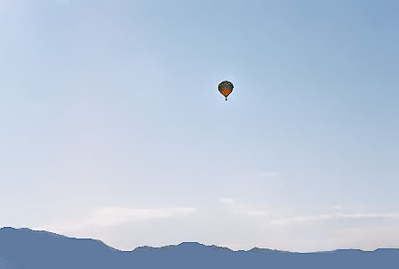 [Multi-colored balloon high in the blue sky above the mountain range.]