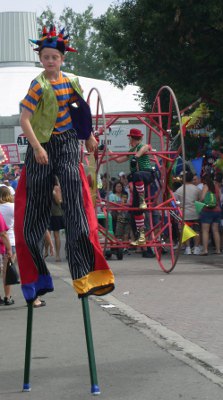 [Young teen in costume and on stilts walking along the parade route.]