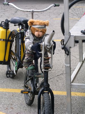 [Stuffed bear in camo clothing attached to the front seat of a two person watergun bike.]