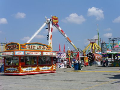 [Candy apple vendor with carnival rides in background.]