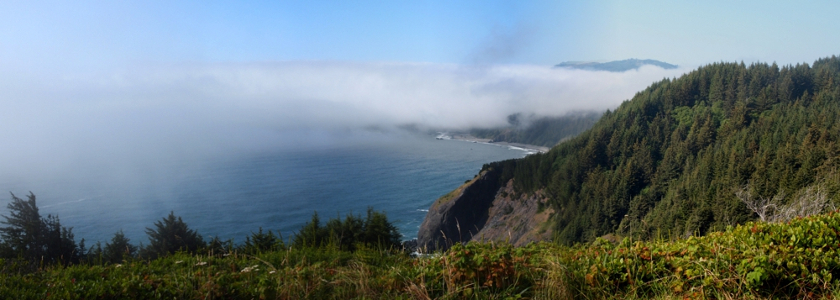 [An expanse of clouds runs through the middle of the photo and blankets part of the ocean shore at this bay. The near ground and that to the right is clearly visible while the distance shore is covered by clouds.]