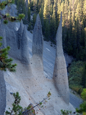 [Several tall, think rock formations coming out of the hillside. Lower level is sand colored while top, pointed portion is a dark ash color.]