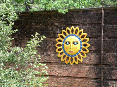 [Colorful sun sculpture hanging on a brick wall.]