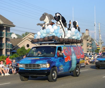 [Aquatic animal costumed characters amid blue and white balloons atop a van advertising the aquarium.]