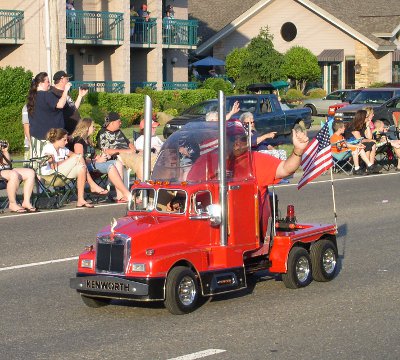 [Man driving mini red truck with exhaust pipes up the sides.]