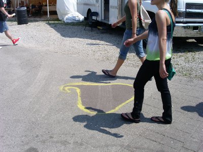 [People walking over a brown morsel outlined in yellow on the pavement.]